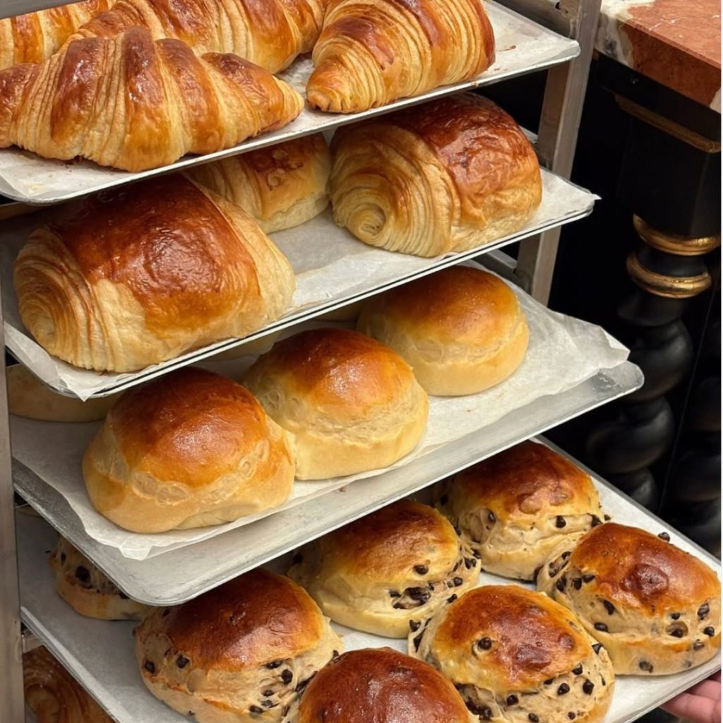 Golden-brown croissants and pain au chocolat cooling on racks at Aux Merveilleux de Fred, one of the best bakeries & patisseries in Dubai.
