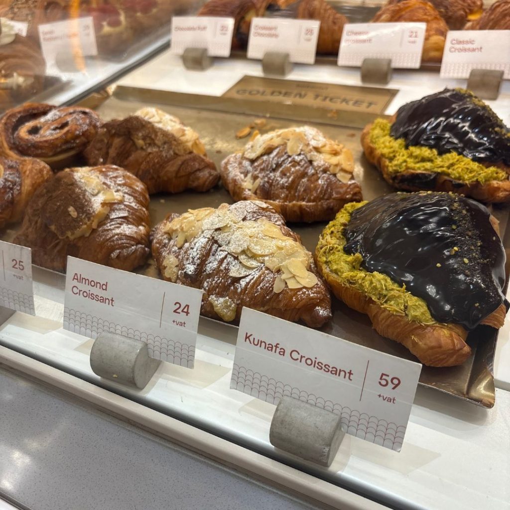 Colourful array of flaky pistachio and chocolate croissants behind a glass counter at Bakerist, artisan patisserie in Dubai.