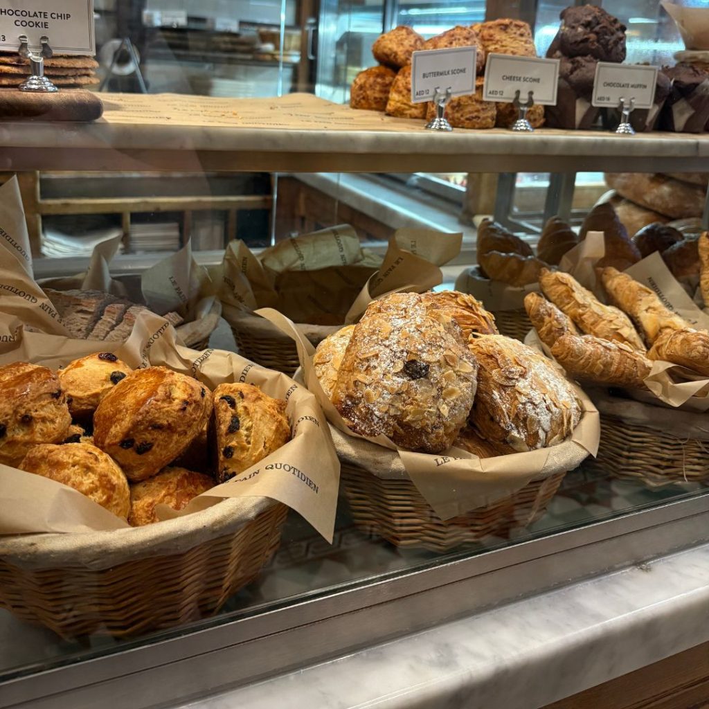 Rustic bread baskets and viennoiserie on wooden shelves at Le Pain Quotidien, classic French bakery chain in Dubai.
