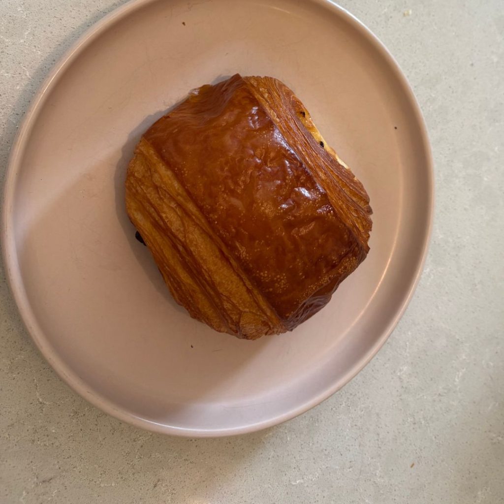 Buttery pain au chocolat on minimalist ceramic plate at Paus; Wellness + Community, cosy café bakery in Jumeirah, Dubai.
